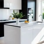 A bright kitchen with a white island and black base surrounded by black and white cabinets and appliances.